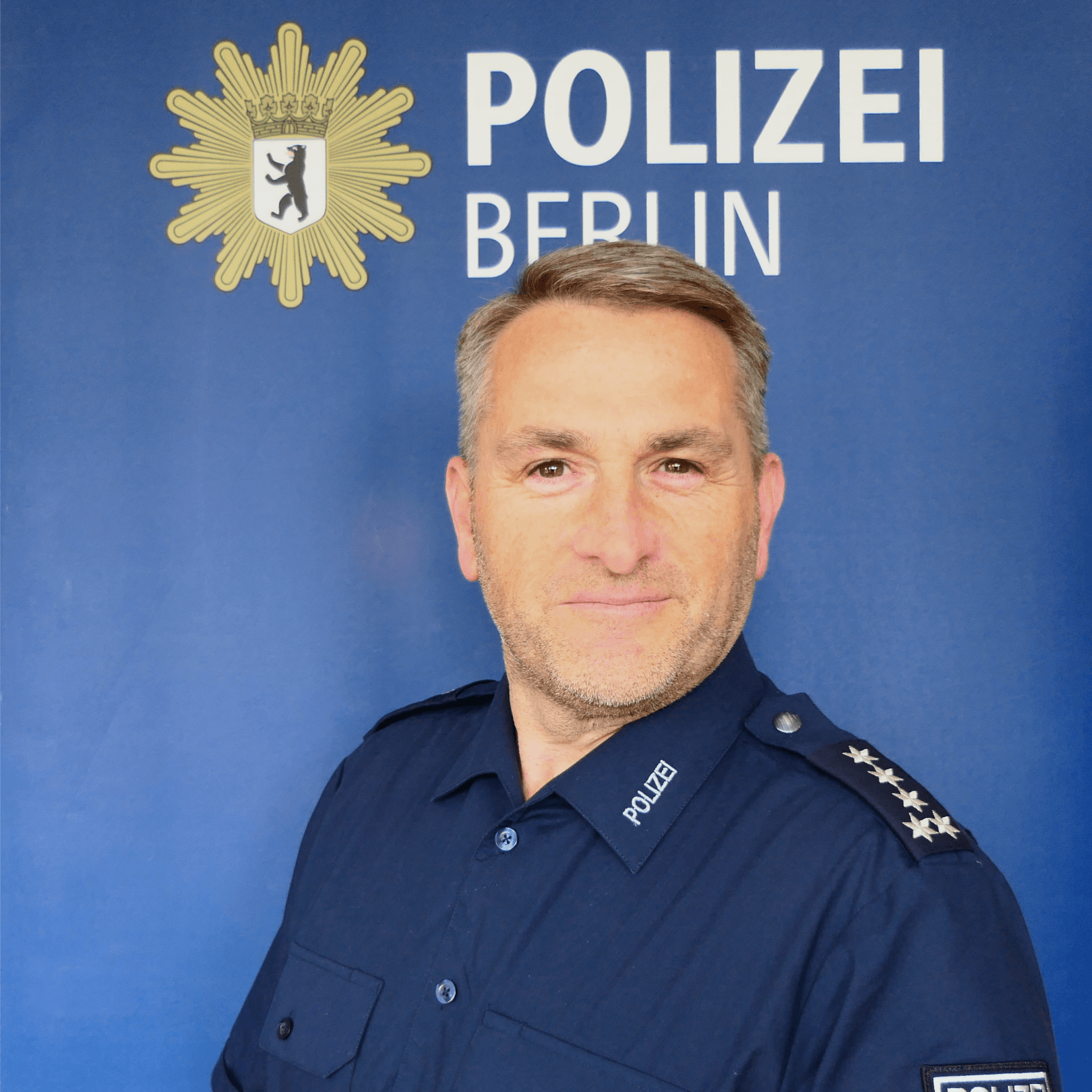 Ein Mann in blauer Uniform lächelt in die Kamera. Er ist Oliver Woitzik von der Berliner Polizei.