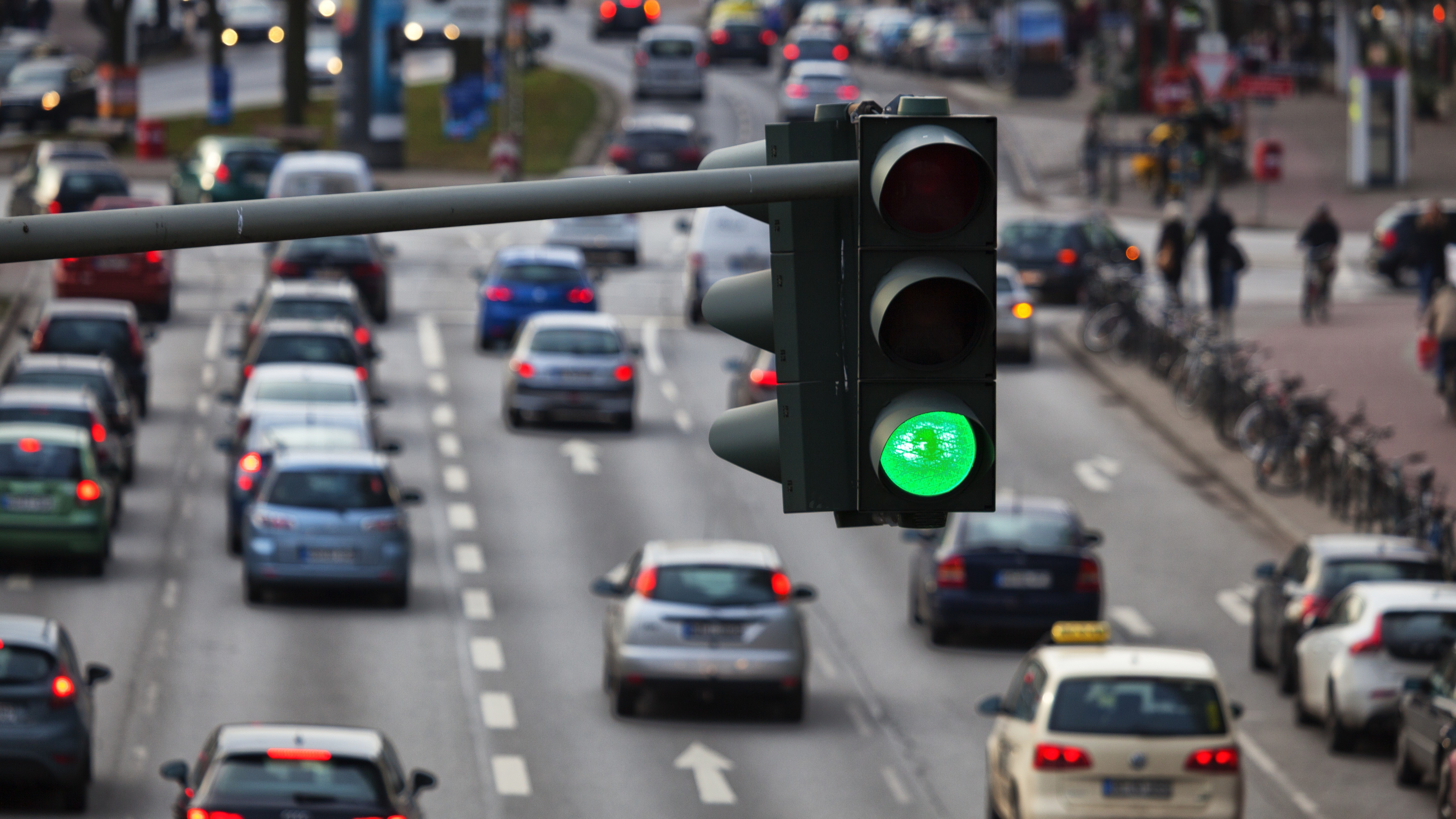Eine Verkehrsampel leuchtet grün. Im Hintergrund sind viele Autos im Stadtverkehr zu sehen.
