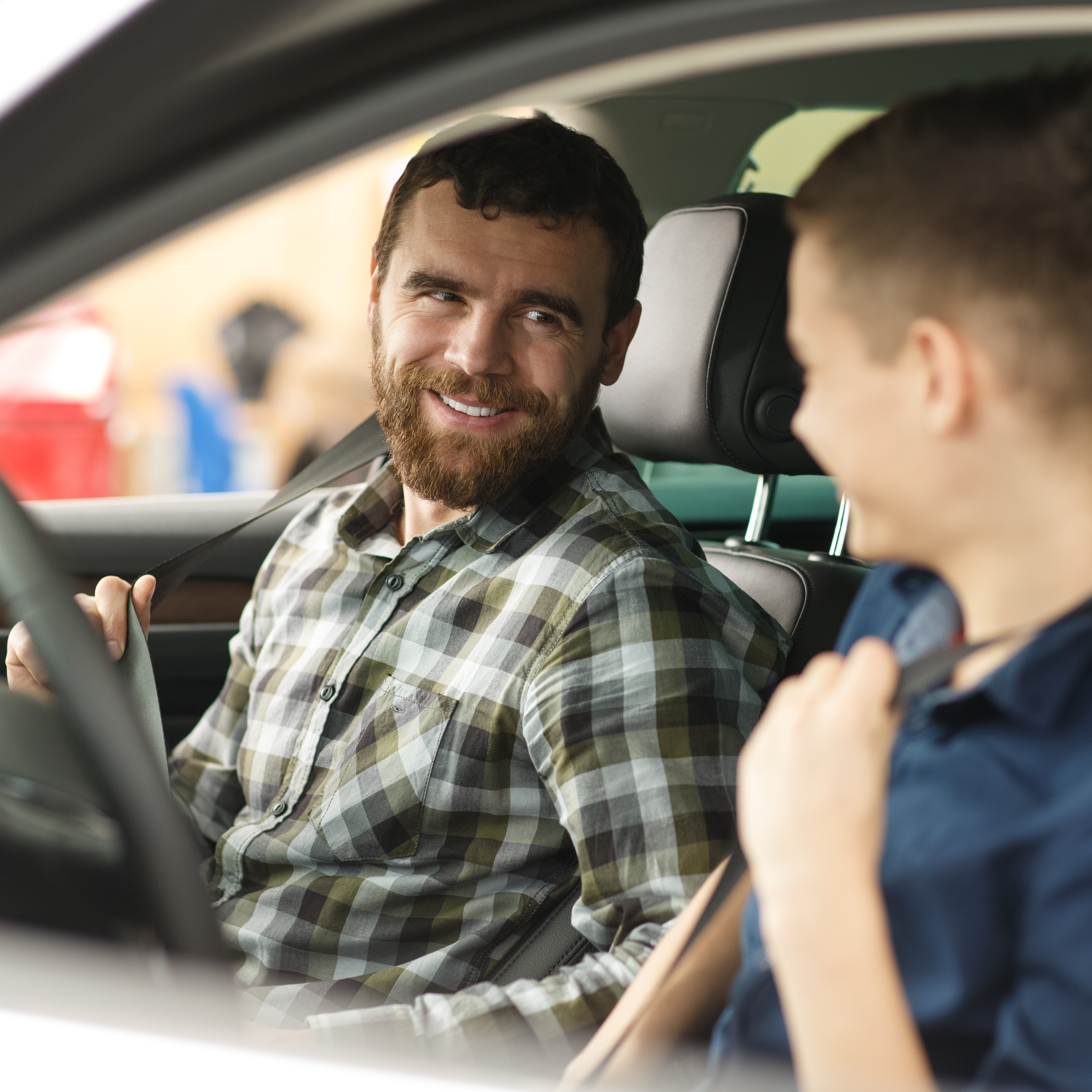 Ein junger Mann und sein Begleiter sitzen in einem parkenden Auto und schnallen sich gerade an.