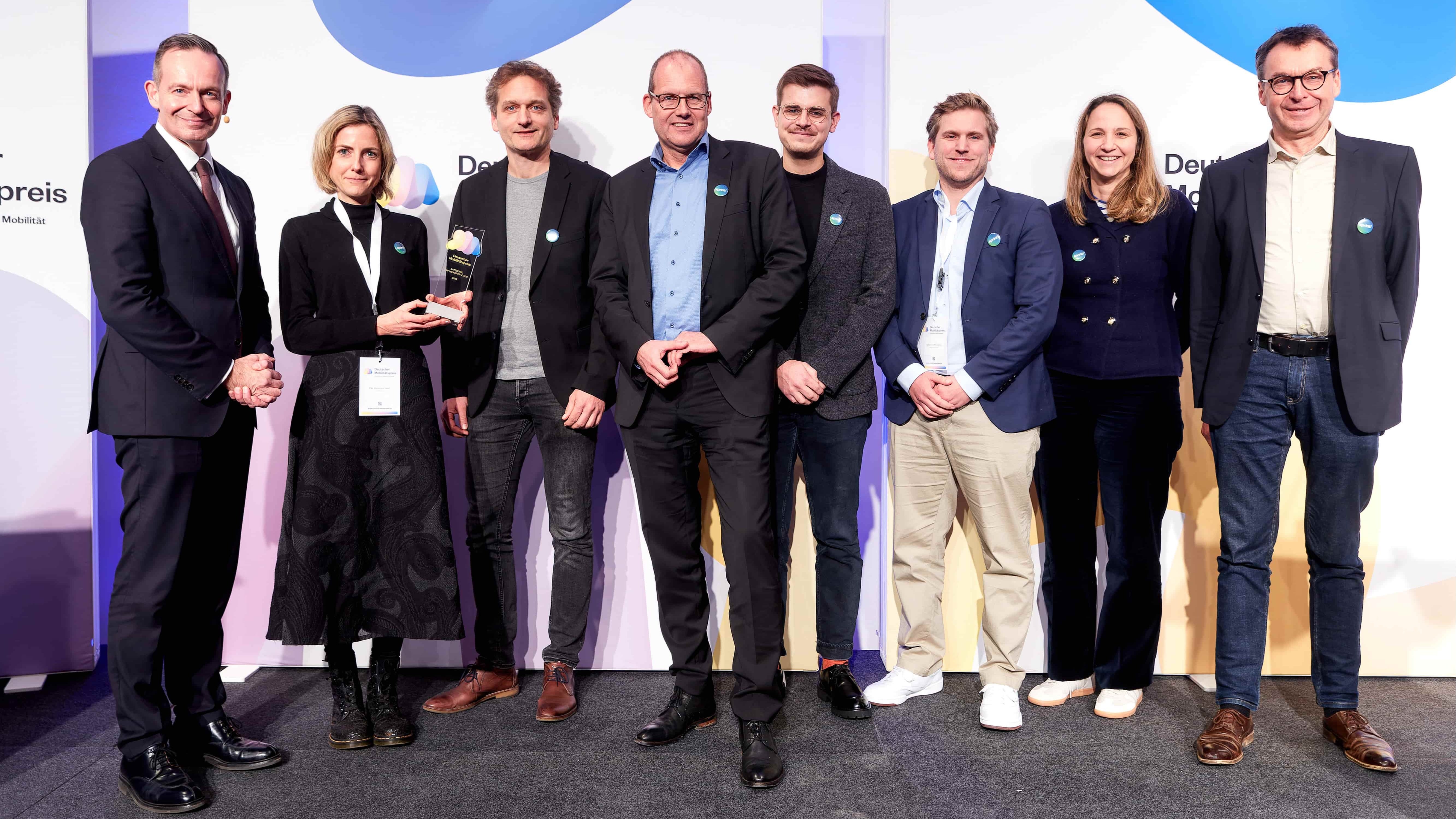 Bundesverkehrsminister Dr. Volker Wissing mit dem Team von sprinti. Alle Personen stehen vor einer hellen Fotowand und lächeln in die Kamera.